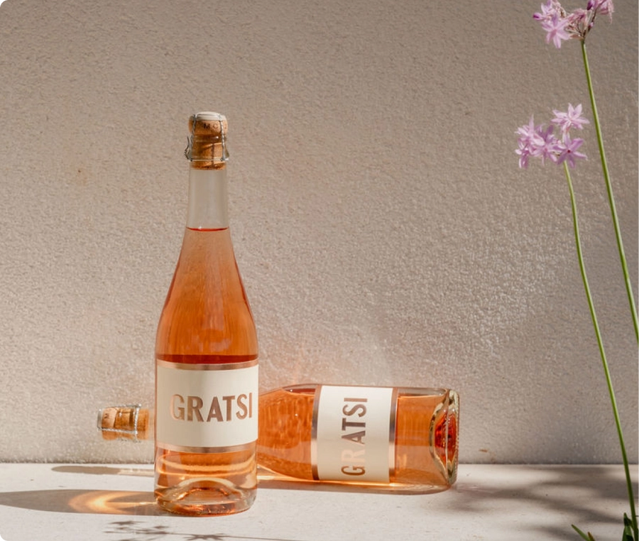 Two bottles of Gratsi sparkling rosé lying and standing beside a small bunch of flowers