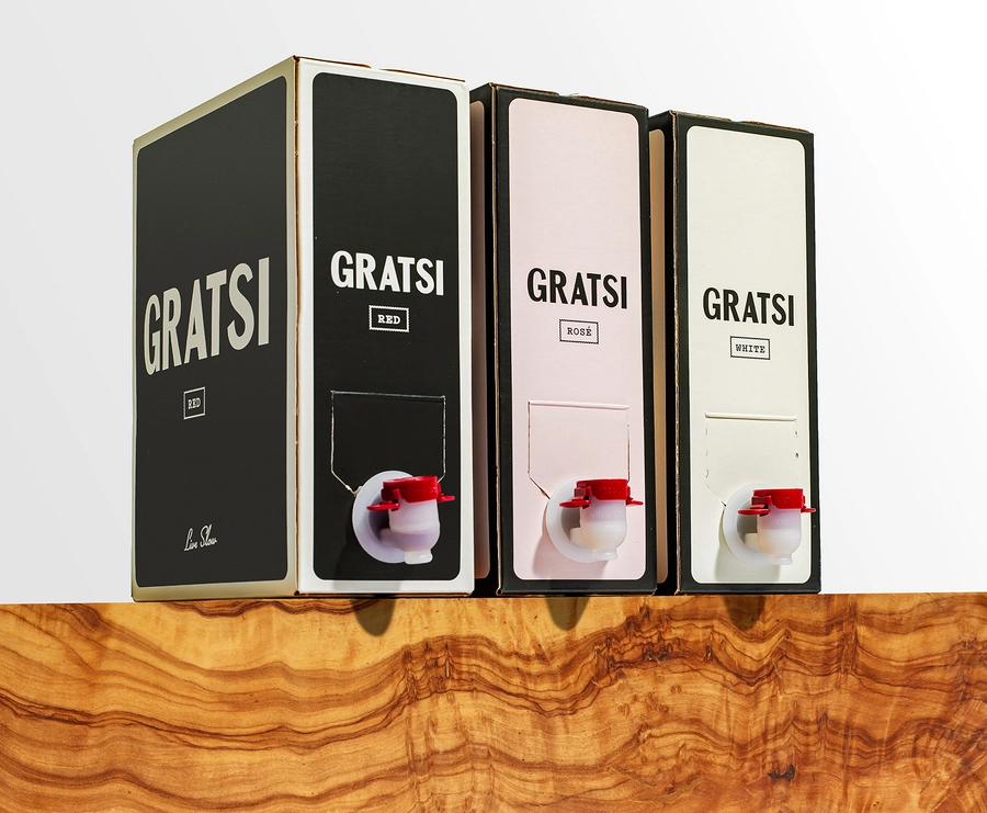 Three boxed wines labeled Gratsi in black, pink, and white packaging for red, rosé, and white wine are displayed on a wooden surface with a white background. Each box has a red spout for pouring.